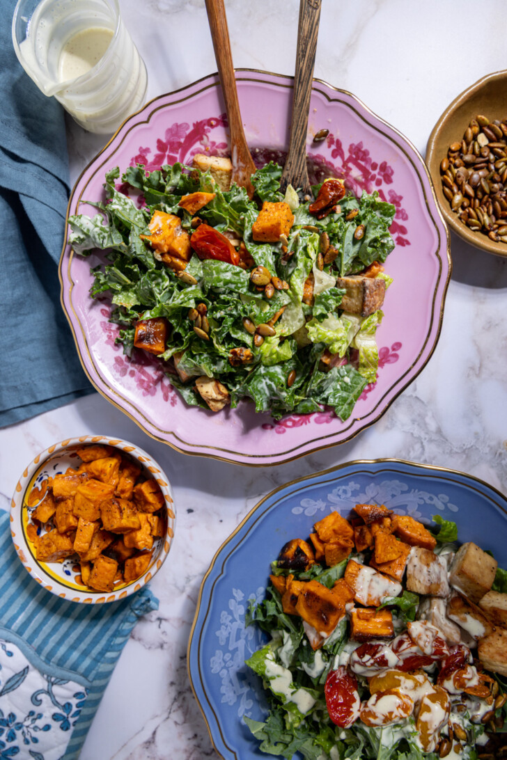 Overhead view of a vegan autumn Caesar salad with kale, romaine, roasted sweet potatoes, tofu cubes, and pumpkin seeds on a vintage plate.