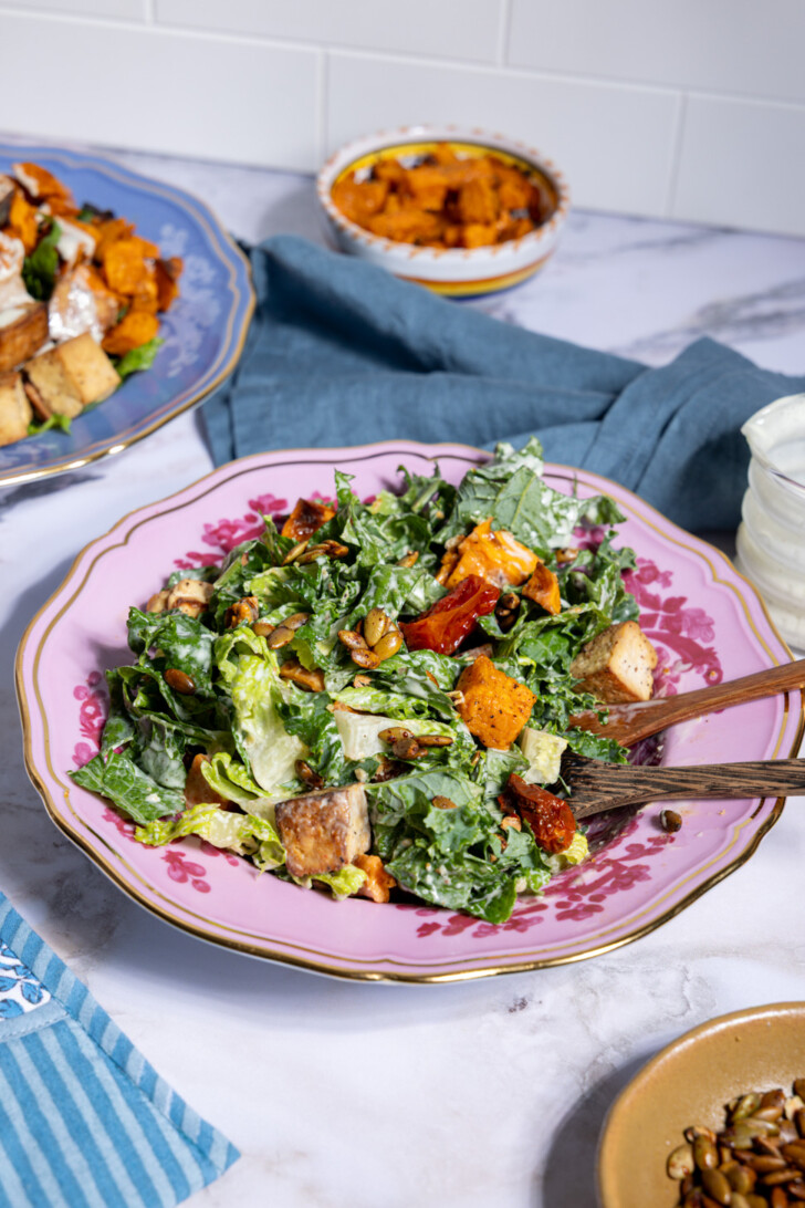 Cozy vegan fall salad styled with sweet potatoes, tofu, and creamy Caesar dressing alongside extra roasted vegetables and pumpkin seeds.
