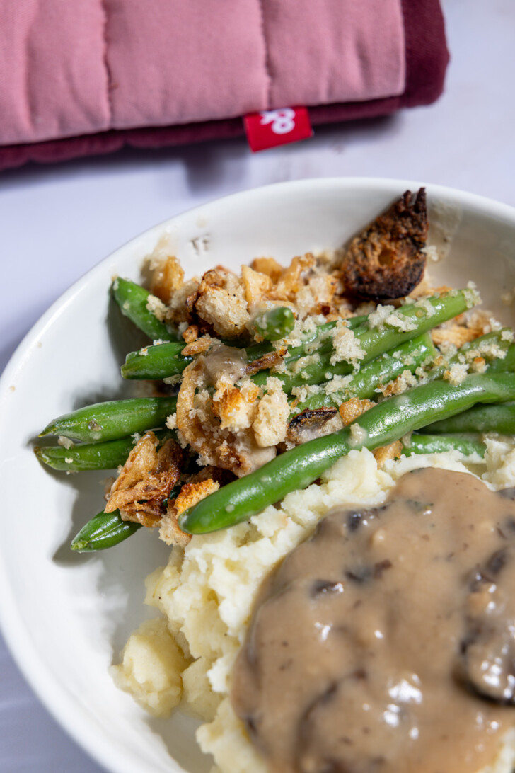 “\Close-up of vegan green bean casserole served with mashed potatoes and mushroom gravy.