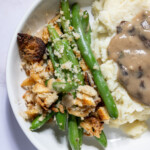 Bowl of vegan green bean casserole with crispy topping next to mashed potatoes.