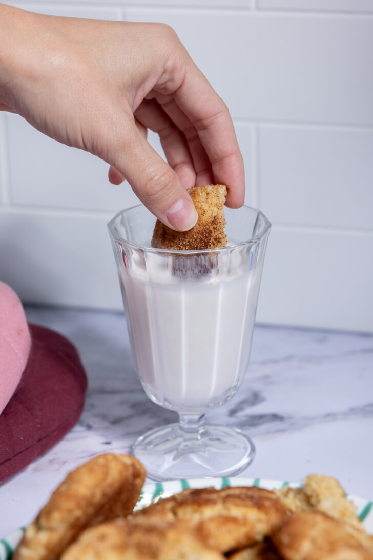 Vegan snickerdoodle cookie being dipped into a glass of plant milk