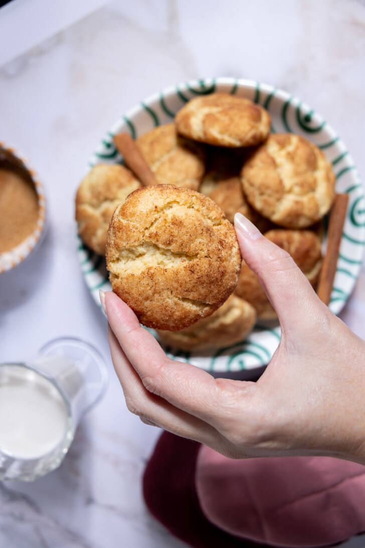 Vegan snickerdoodle cookie held by hand over a plate of cookies